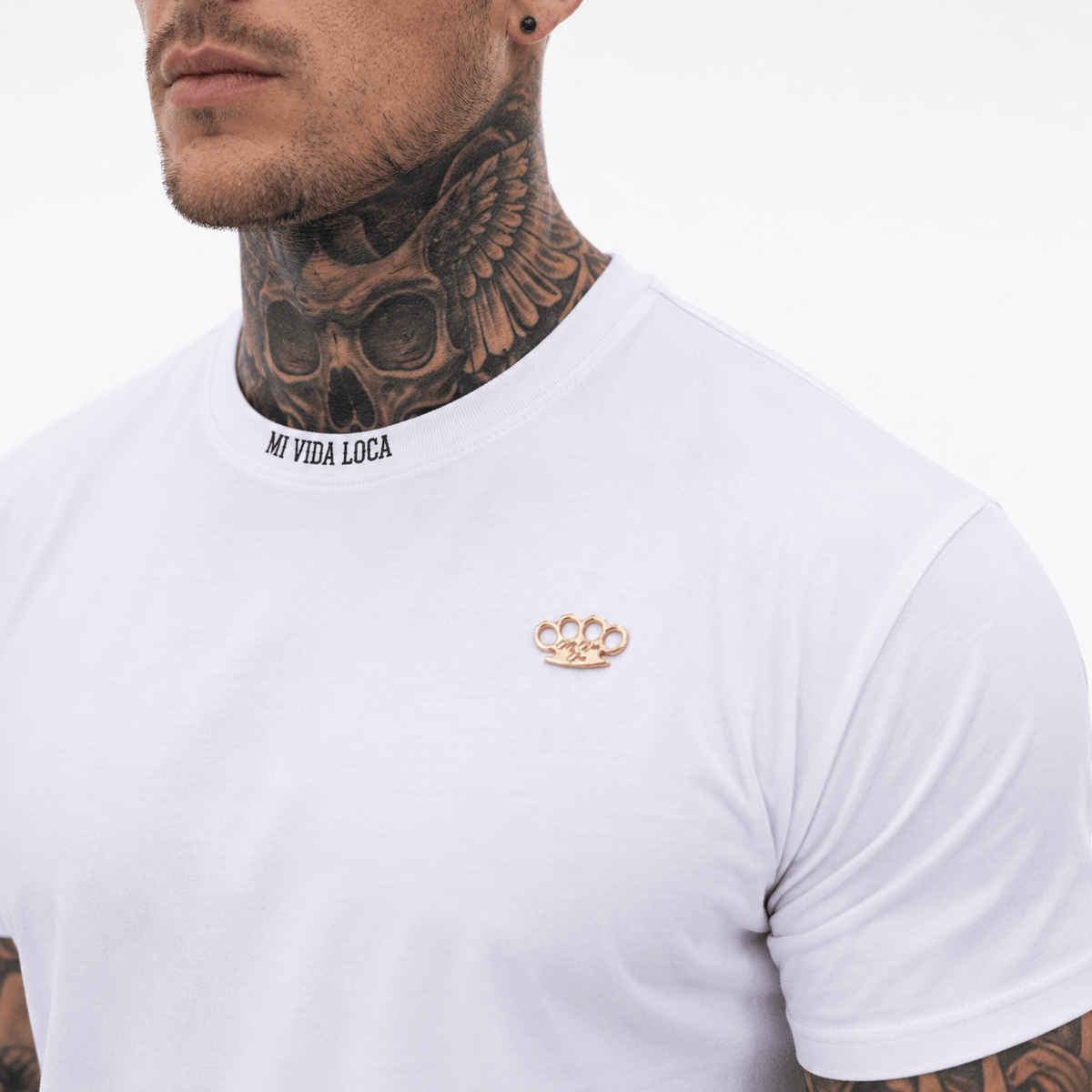 Close-up van de kraag van het Trust nobody T-shirt wit met Mi Vida Loca tekst en gouden MVL logo op de borst