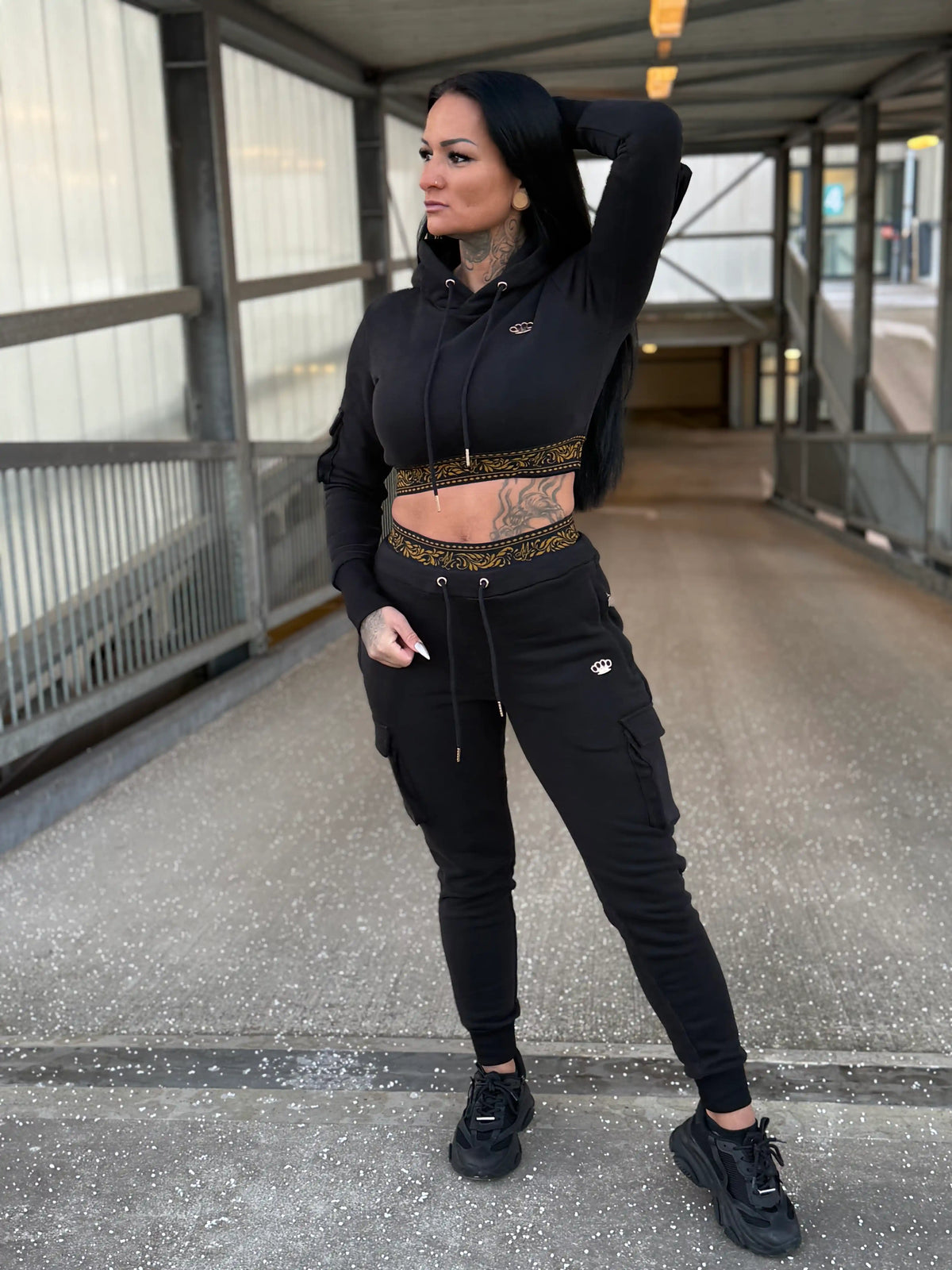 Model in the black MVL Meander women's tracksuit with cropped hoodie on a footbridge