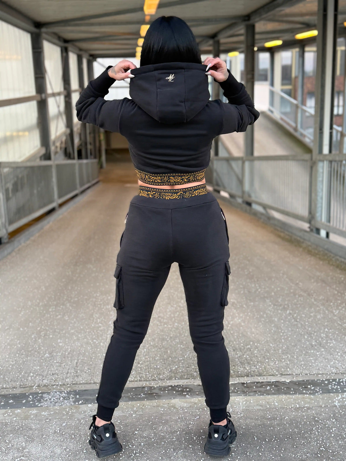 Back of the cropped MVL Meander women's hoodie with the hood up, model on a footbridge