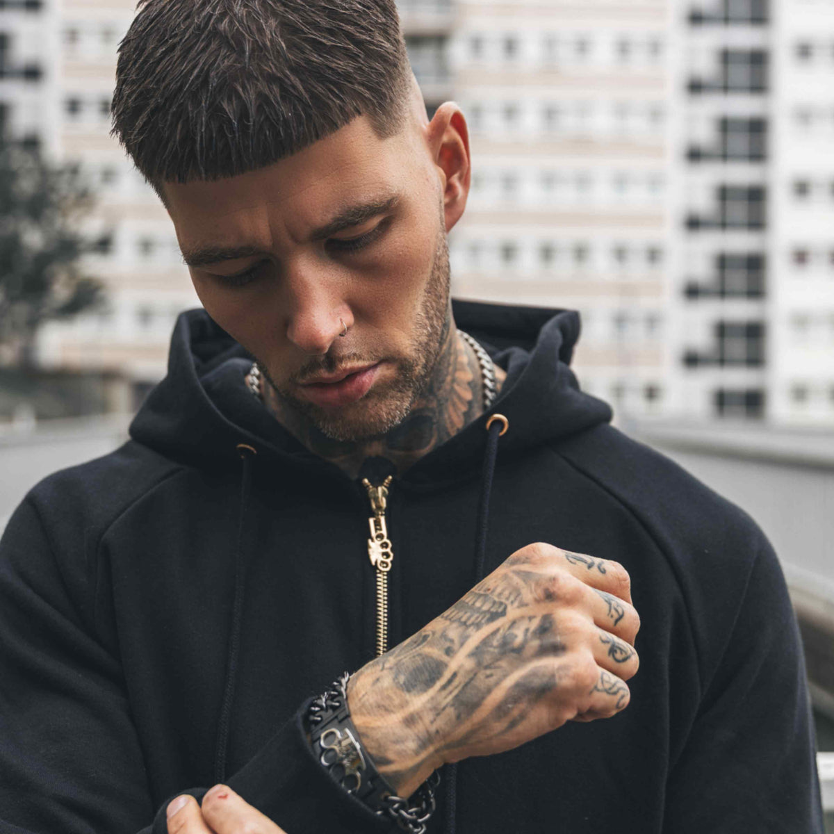 Close-up van de zwarte Cupid with gun hoodie met gouden rits, gedragen door getatoeëerd model