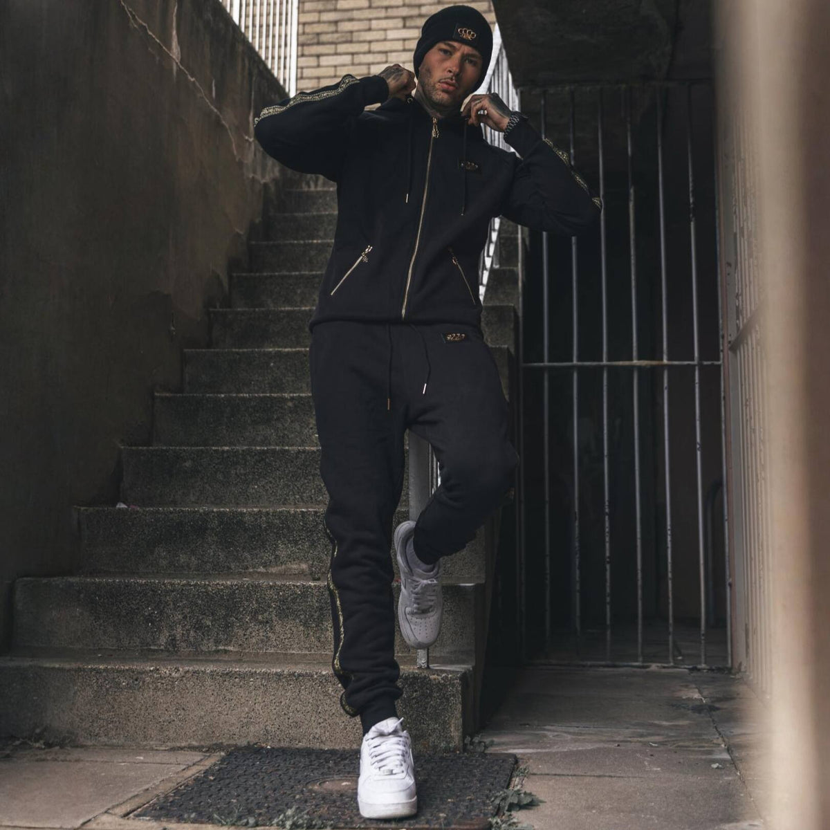 Model in MVL Meander hoodie en joggingbroek op een buitentrap, met witte sneakers