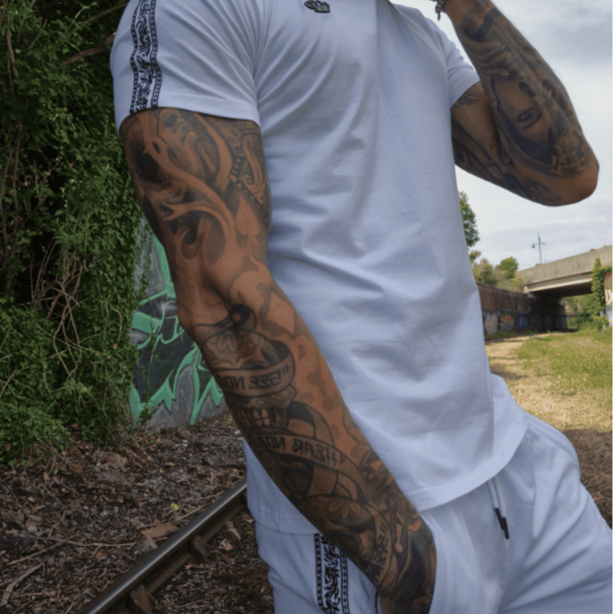 Model i hvid MVL T-shirt og hvide Meander shorts ved togskinner med graffiti
