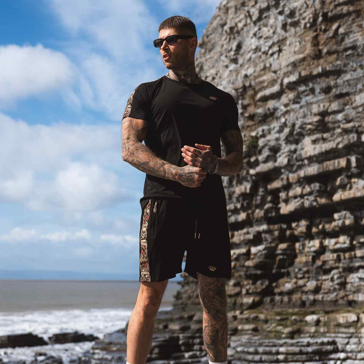 LFR jogger shorts in black worn by a model with a black T-shirt by the rocks at the sea