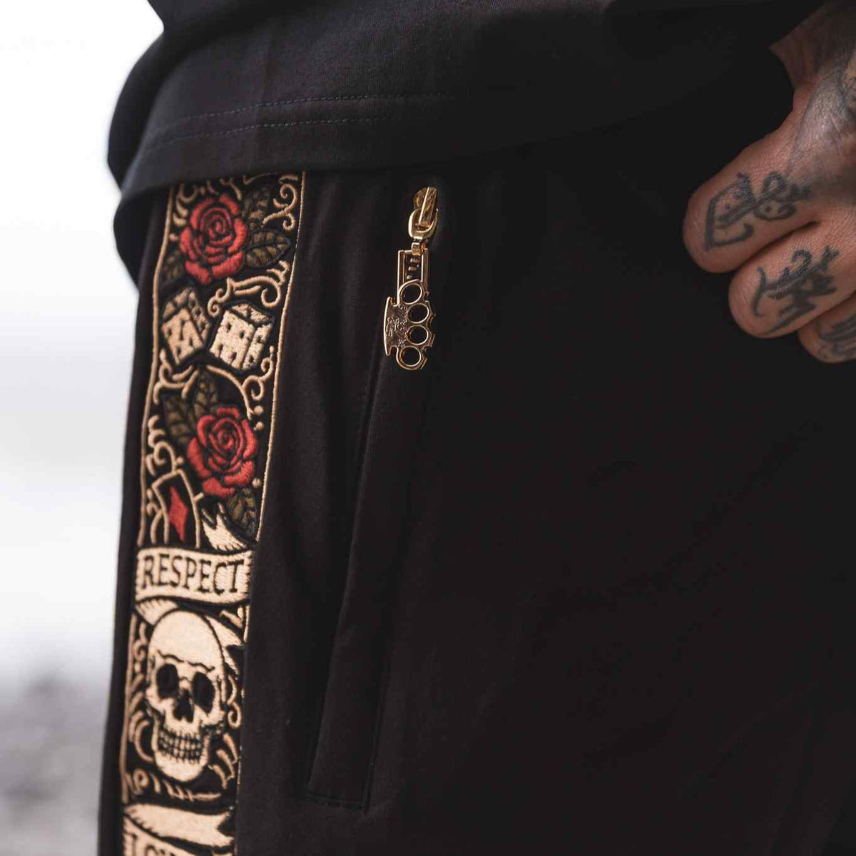 Detail of the black LFR jogger shorts: zip with gold MVL logo pendant next to the embroidered band