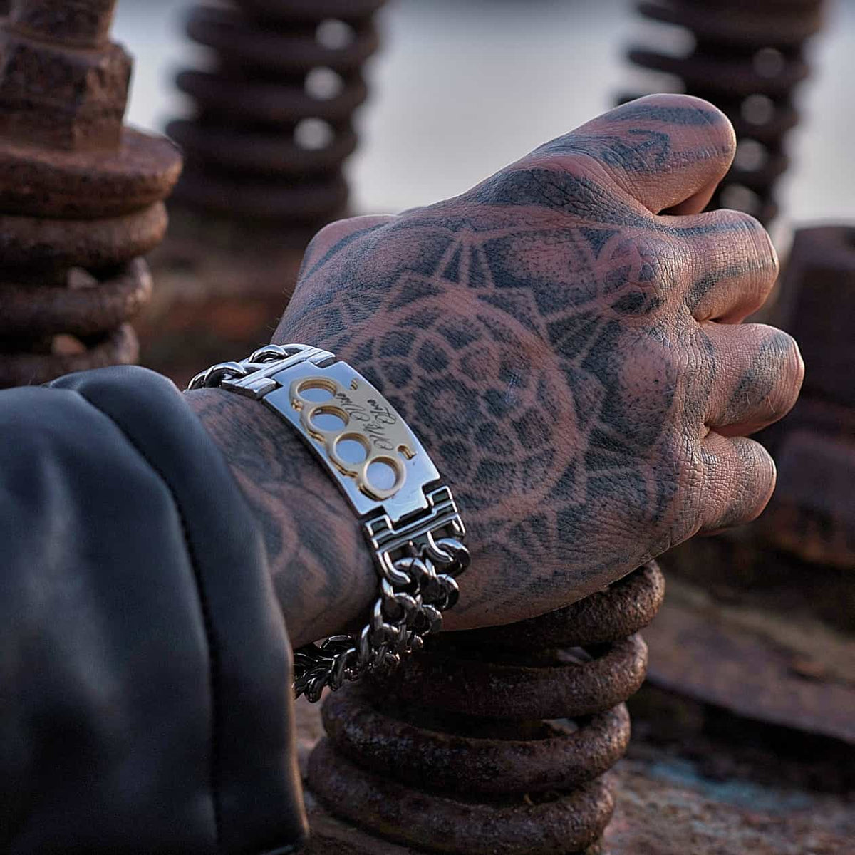 MVL armbånd i sølv/guld om en tatoveret hånd på rustne metalspiraler