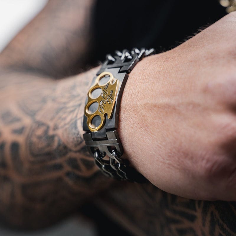 MVL Armband schwarz/gold am Handgelenk eines tätowierten Arms, goldenes MVL-Logo im Bild