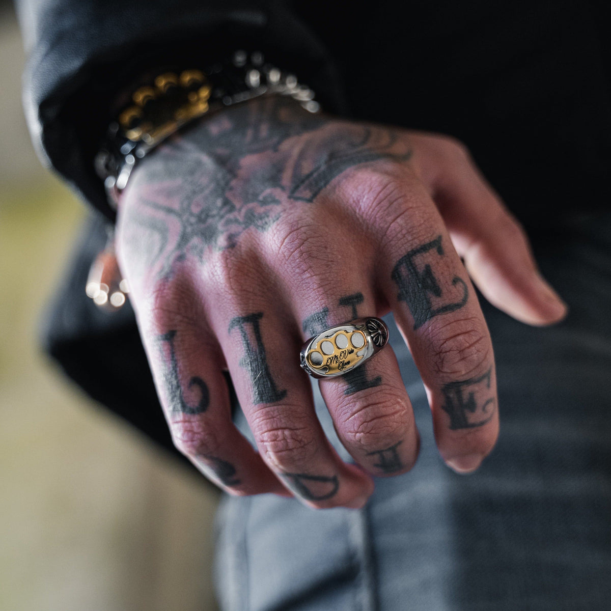 MVL Logo ring in silver on the finger of a tattooed hand, close-up