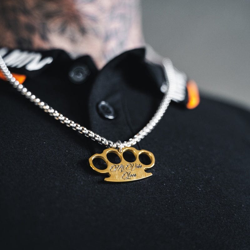 MVL Logo necklace in silver/gold worn over a black shirt, close-up of the pendant